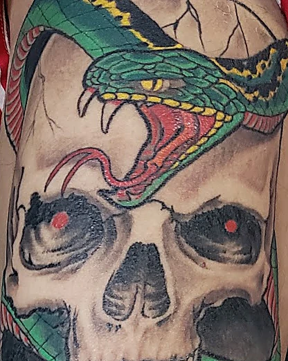 Tatuaje a color de una serpiente verde enroscada sobre una calavera con ojos rojos en la pierna