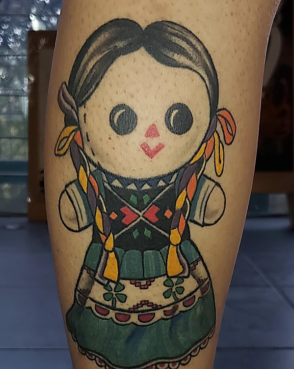 Tatuaje de muñeca mexicana de trapo con trenzas de listones y vestido verde en la pantorrilla